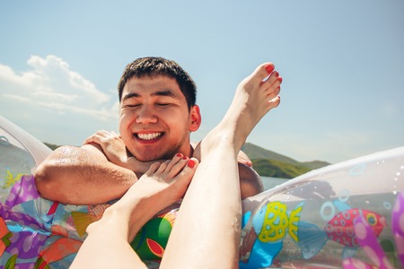 smiling Man with inflatable rubber ring at sea and legs of womanの写真素材