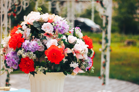 artificial flowers in a ceramic pot and watering can standing on a metal table outdoorsの写真素材