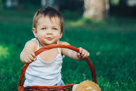 Smiling happy child with basket sitting on green grass in summer parkの写真素材
