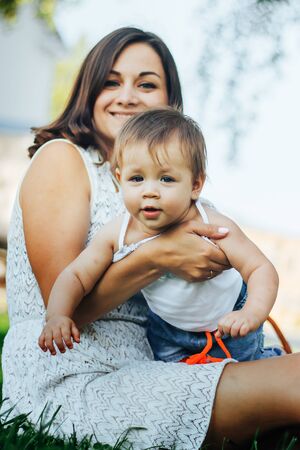 Portrait of happy little mom kissing and shake baby outdoors on green summer garden with fresh green...