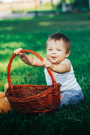 Smiling happy child with basket sitting on green grass in summer parkの写真素材