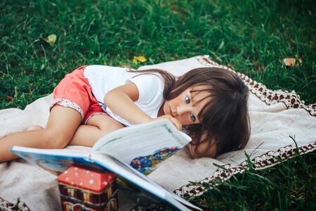 little girl lie on grass and reading bookの写真素材