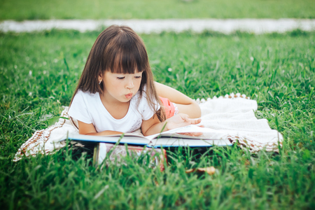 little girl lie on grass and reading bookの写真素材