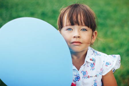 little girl with blue eyes and blue baloon looking at cameraの写真素材