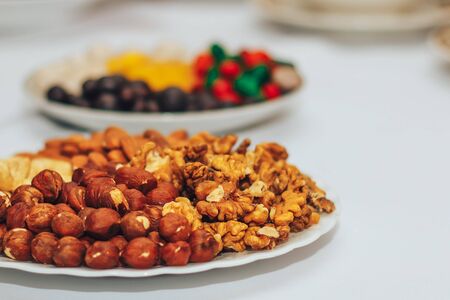 Assortment of nuts on a white plate and on a white background wooden boards. Background of nuts. View from above.の写真素材