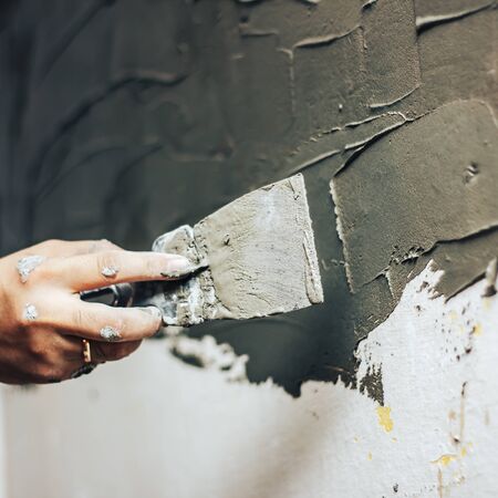 work aligns with a spatula Worker working manual with wall plastering tools inside a officeの写真素材