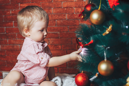 baby touching chistmas toys on christmas tree, he try to put ball on the treeの写真素材
