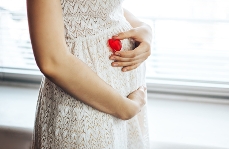 Pregnant woman holding a hearth shape on her bellyの写真素材