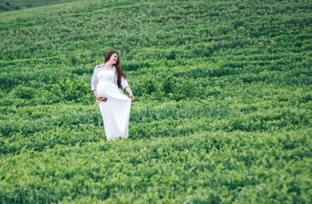 pregnant women in green field in white dressの写真素材