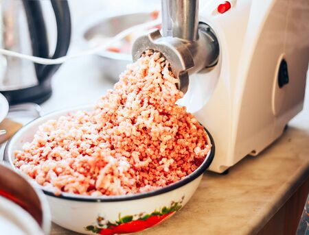 electric meat grinder with a tray for meat and a metal pipe twists meat for cutlets, a plate with ready forcemeat nearby.の写真素材