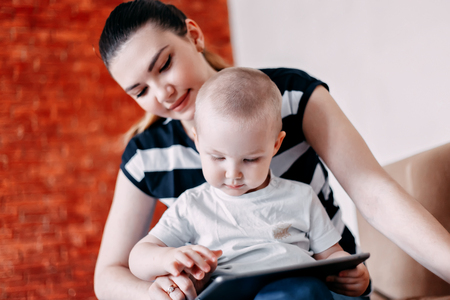 Mother and baby are looking to play and read tablet computer at home.の写真素材
