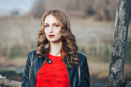 beautiful young girl red hair in red sweater and red dress with makeup and hairdress outdoors in spring forestの写真素材