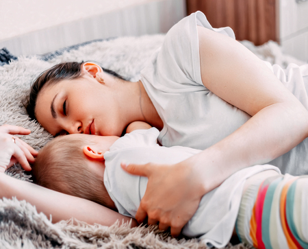 Side view of beautiful young mom and her cute little baby sleeping in bed at homeの写真素材