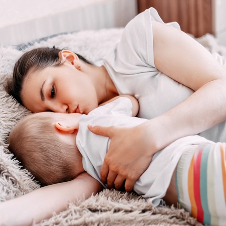 Side view of beautiful young mom and her cute little baby sleeping in bed at homeの写真素材