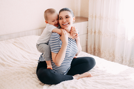 cute blonde little boy hugging a pregnant mother's belly at home, indoor. Mother and son plays in expecting their second child.の写真素材