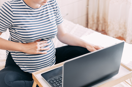 Pregnant woman working on laptop. Cropped image of pregnant businesswoman typing something on laptop while sitting at her working place at homeの写真素材