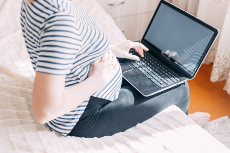 Pregnant woman working on laptop. Cropped image of pregnant businesswoman typing something on laptop while sitting at her working place at homeの写真素材