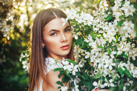 Pretty girl portrait near blossomed tree in park. Concept of youth and natural beauty. Young girl smells scent of cherry blossoms in spring in the garden. Woman and spring nature, natural cosmeticsの写真素材