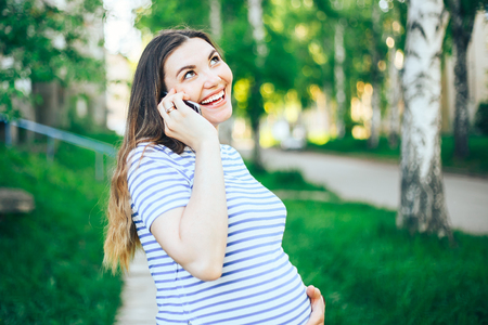 Happy pregnant girl talking on phone at sunset in blooming spring park. pregnant girl with phone lit by rays of sunの写真素材