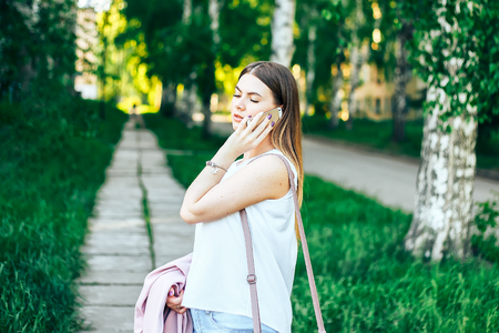 technology, lifestyle, communication and people concept - smiling young woman or teenage girl calling on smartphone on city streetの写真素材