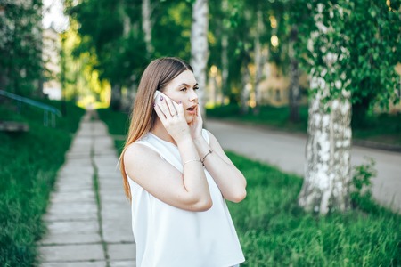 Young shocked woman walking in park while talking by phoneの写真素材
