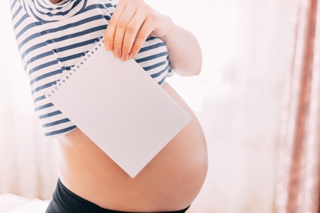 Cheerful pregnant woman making notes in jotter, focuse on paper, belly is unfocusedの写真素材