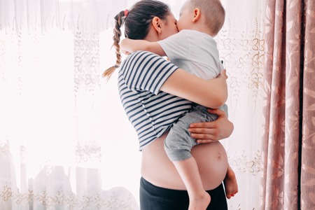 Beautiful pregnant woman and her toddler son. Young mother waiting of a second baby. Pregnancy and family image. Elder brother waiting little baby.の写真素材