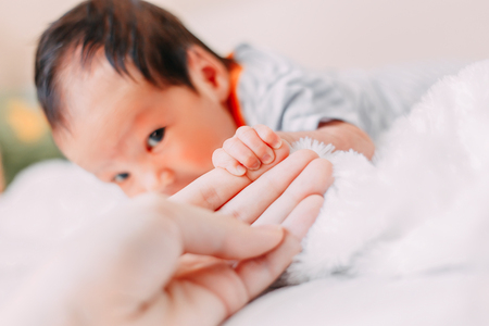 Close-up shot of baby's little cute hand reaching for mother's loving hand. While holding her finger she caresses his hand.の写真素材