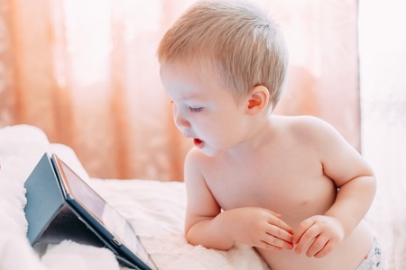 Portrait of a little boy who is watching a funny cartoon on a tablet and laughs. A child is playing on the tablet at home and smiling.の写真素材