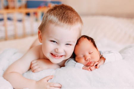 Happy little brother with newborn baby lying in a bed together, kissing and hugging. Siblings. New born baby sleeping and two years old brother together. Love. Family.の写真素材