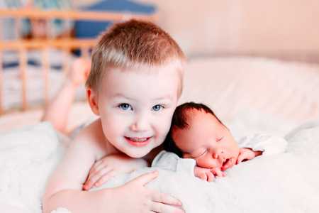 Happy little brother with newborn baby lying in a bed together, kissing and hugging. Siblings. New born baby sleeping and two years old brother together. Love. Family.の写真素材