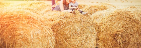 Mom and son at sunset sit in a field on a haystack and hug against the setting sun. Rural life, a walk in nature, a holiday in the countrysideの写真素材