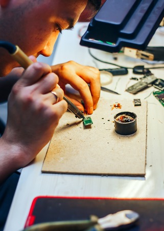 young man teenager soldering computer circuit with soldering iron at home. brazeの写真素材