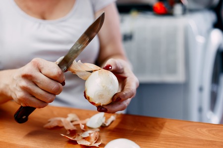 Young housewife beginner cook cutting onion. Slice,dice and chop onion. Shedding tears and wiping with the back of her hand.の写真素材