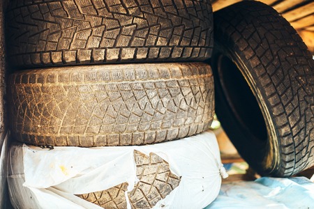 A pile of old, worn tires. They are dirty and the rims are rusty. The tire in the center is coated with light mud.の写真素材