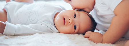 Cute little baby with elder brother lying on bed at home long bannerの写真素材