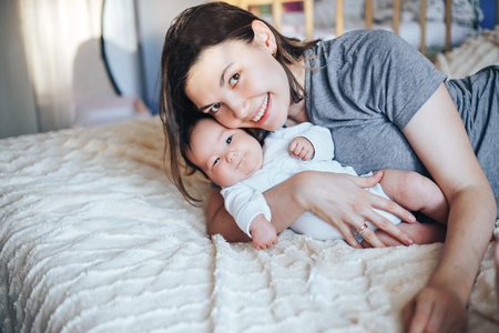 Smiling young woman with book and baby on a bedの写真素材