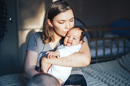 Smiling young woman with book and baby on a bedの写真素材