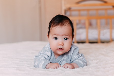 baby, newborn baby cute blue-eyed, dark hair, baby 2 months in a blue body lying on his stomachの写真素材