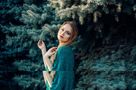 portrait of beautiful blue eyed red haired smiling girl in knitted sweater posing in front of snow covered firtrees. Fairytale conceptの写真素材