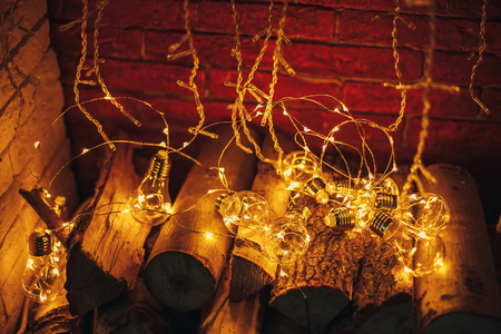 decoration gerland christmas lights bulb lying in fireplace on wooden firewood loft design fireplace of whote brickの写真素材