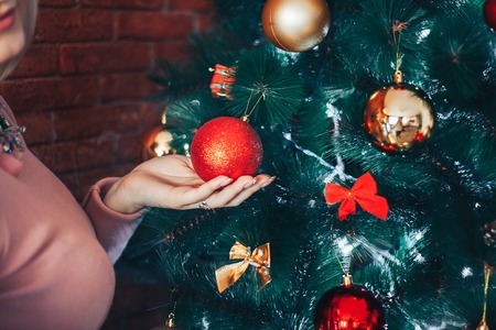 Close-up of a branch of a Christmas tree with bright toys. Human hands holding a pred ball. The concept of celebration and fun.の写真素材