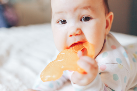 Portrait of a cute 6 month old baby, boy or girl, playing with a teething toy.の写真素材