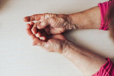 Close-up shot of a senior woman's hands resting on light background. Old lady sitting with her hands clasped on a table. top view copy spaceの写真素材