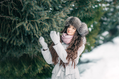 Young beautiful girl in fur hat in winter coat standing near tree spruce long hairの写真素材