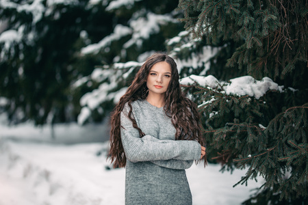 Outdoor close up portrait of young beautiful girl wearing sweater. Elegant model with long dark hair posing in winter forest. Winter holidays concept. beautiful green eyesの写真素材