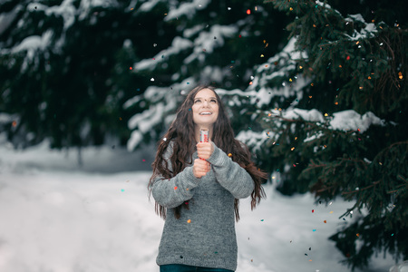 beautiful girl in winter in sweater with long dark hair use petard firecracker near spurce