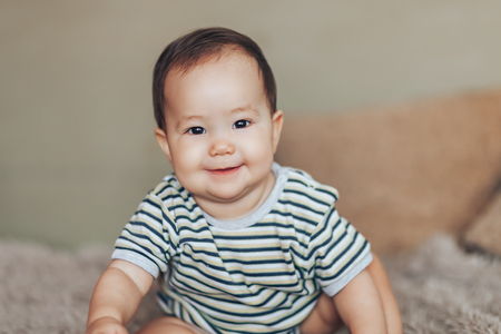 Beautiful smiling baby girl with big dark eyes dark hair sitting at floor and looking up at camera.の写真素材