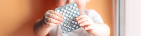 A small child toddler baby boy holds a plate with pills in his hands selected focus on pills kid...