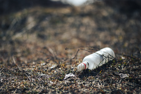 Empty white glass bottle lying on grass in early spring, polluted, conservancy. rubbish after last snows of winter.の写真素材